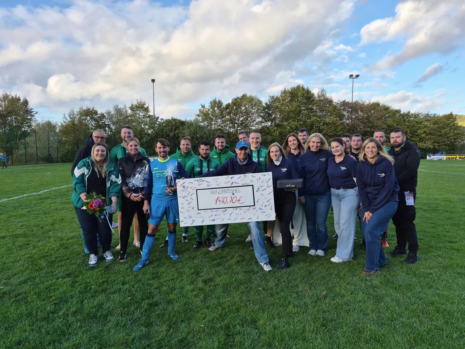 Scheckübergabe auf dem Rasen in Langenbieber: Spieler des TSV in grünen Trikots und das Team von Surgical Mission Saarland halten den unterschriebenen Scheck