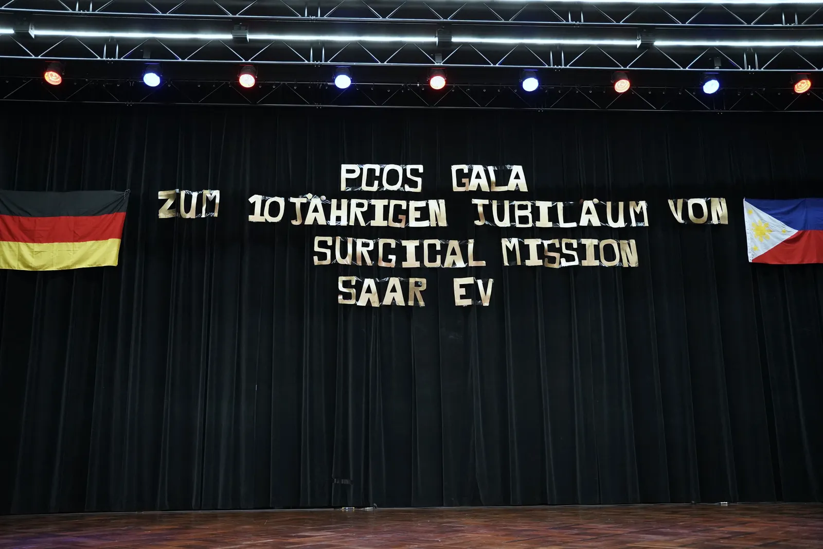 The empty stage of the Stadthalle St. Ingbert with the lettering “PCOS Gala for the 10th anniversary of Surgical Mission Saar e.V.”