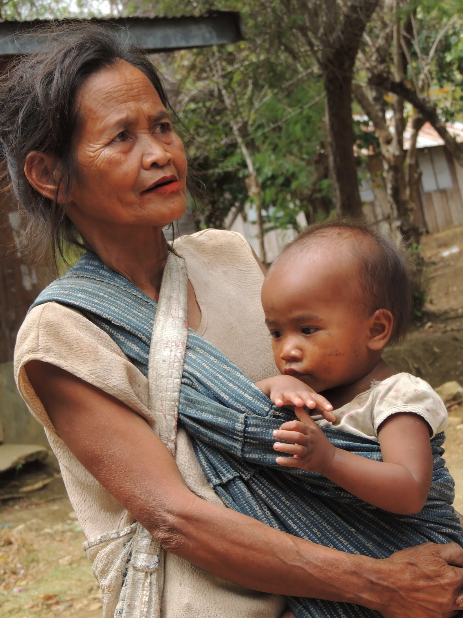 A woman carrying a child in a sling in a village in the Philippines